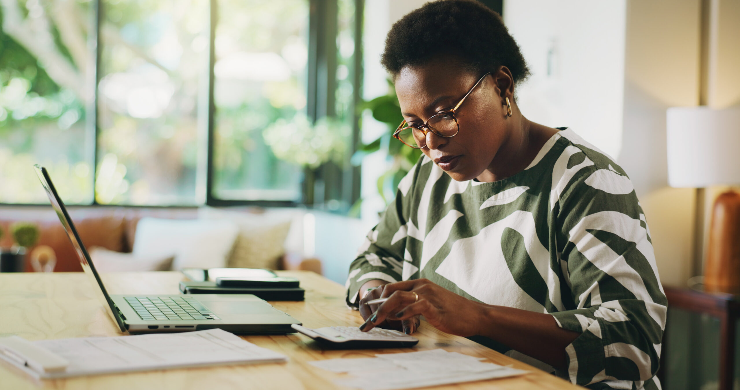 Black woman, finance or laptop with calculator for budget planning, accounting or salary at home. Female person, accountant and remote work on computer for financial audit, expenses or bills at house